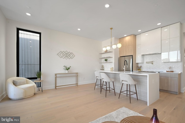 kitchen with pendant lighting, a breakfast bar, a center island with sink, white cabinetry, and stainless steel refrigerator