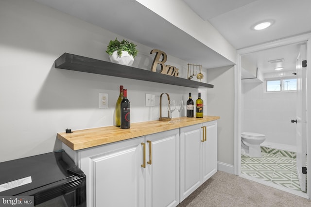 bar with wood counters, light colored carpet, and white cabinetry