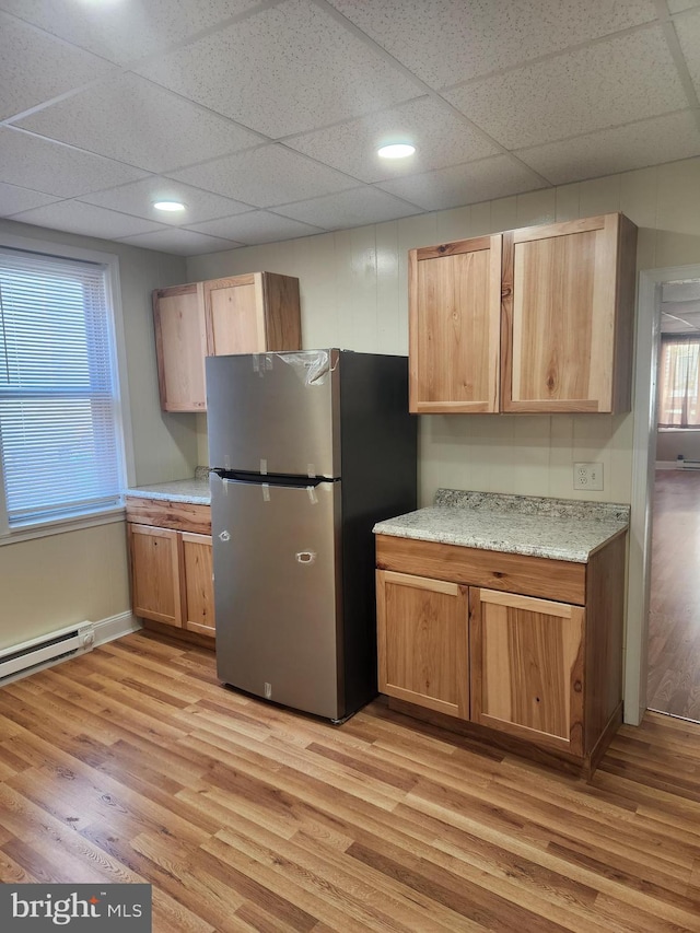 kitchen with a drop ceiling, stainless steel fridge, a baseboard heating unit, and light hardwood / wood-style flooring