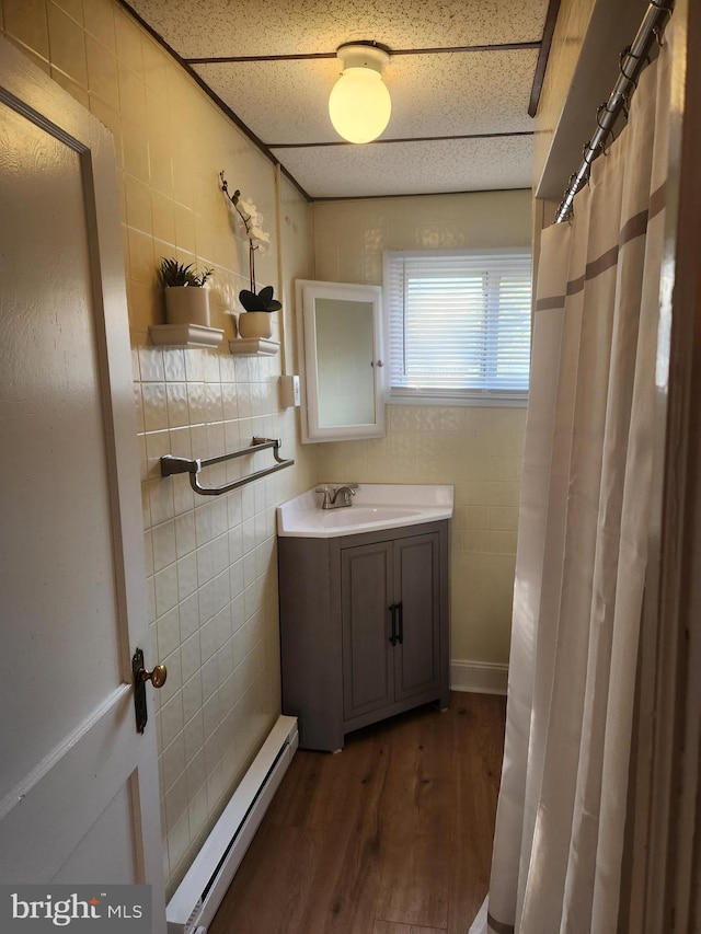 bathroom with a drop ceiling, wood-type flooring, vanity, and a baseboard radiator