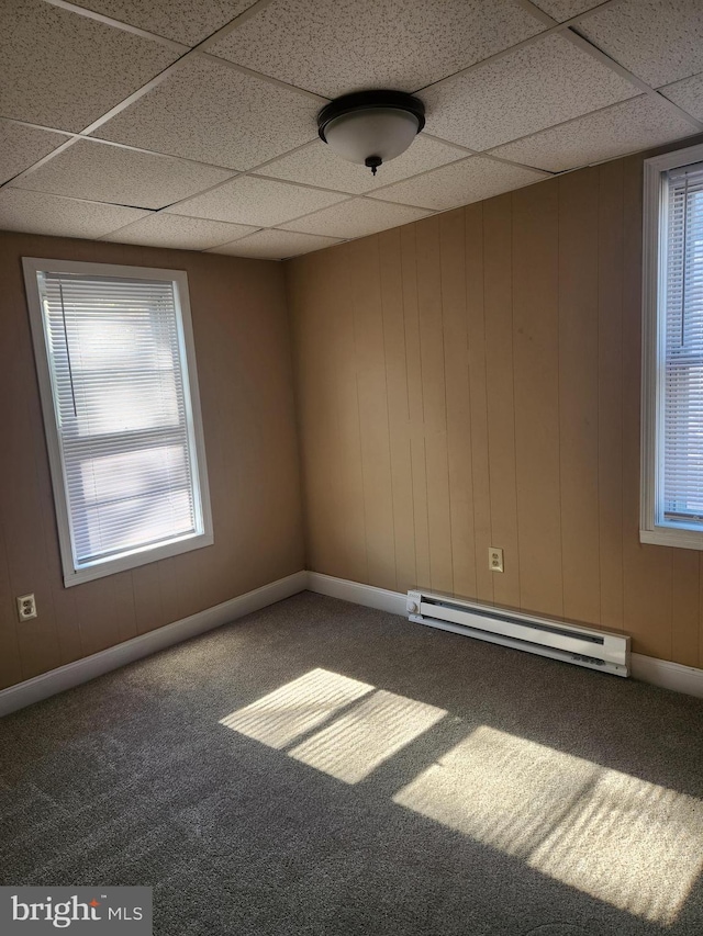 carpeted spare room featuring a paneled ceiling, a baseboard radiator, and wood walls