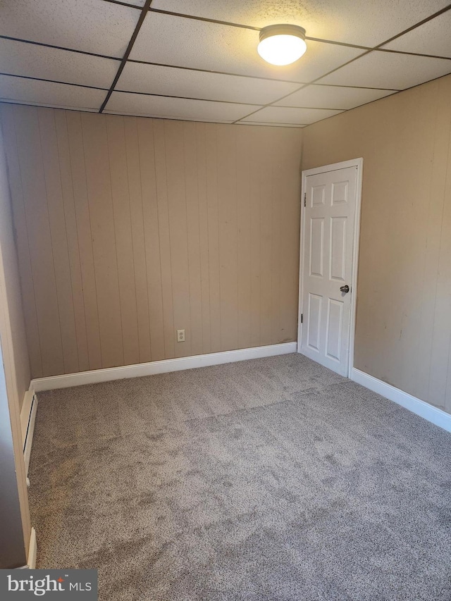 empty room with carpet, a drop ceiling, and wood walls