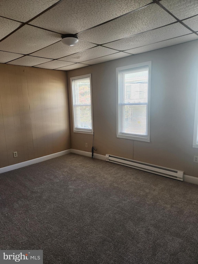 carpeted spare room with a paneled ceiling, a wealth of natural light, baseboard heating, and wooden walls