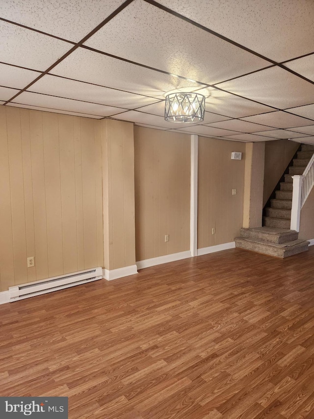 basement featuring a paneled ceiling, a baseboard radiator, and hardwood / wood-style flooring