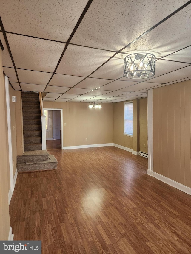 basement with a paneled ceiling, baseboard heating, and hardwood / wood-style floors