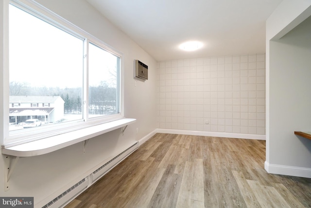 empty room with baseboard heating, light hardwood / wood-style flooring, a healthy amount of sunlight, and a wall mounted air conditioner