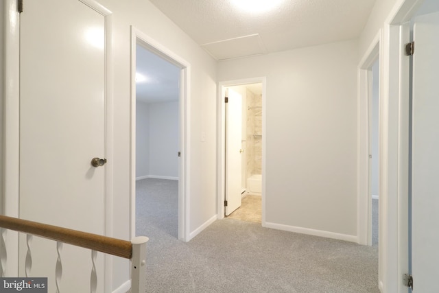 hallway featuring light colored carpet and a textured ceiling