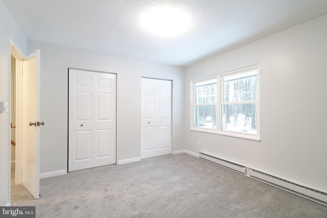 unfurnished bedroom with light carpet, a textured ceiling, a baseboard radiator, and multiple closets