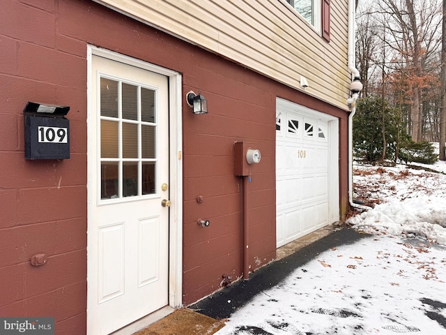 snow covered property entrance with a garage