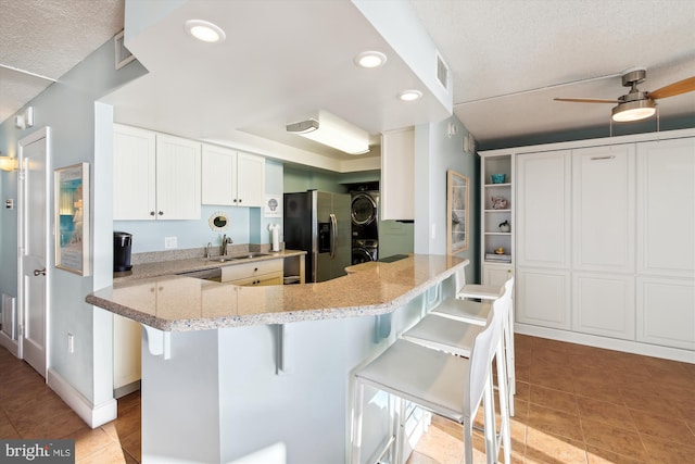 kitchen featuring a breakfast bar, kitchen peninsula, stacked washer / dryer, stainless steel fridge with ice dispenser, and white cabinets