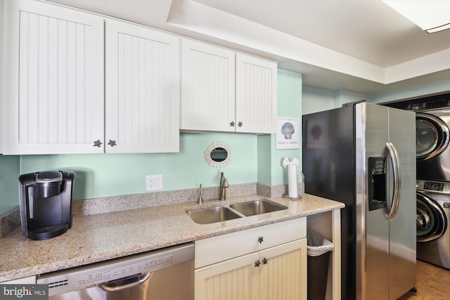 kitchen with stacked washer / drying machine, appliances with stainless steel finishes, sink, and light stone counters