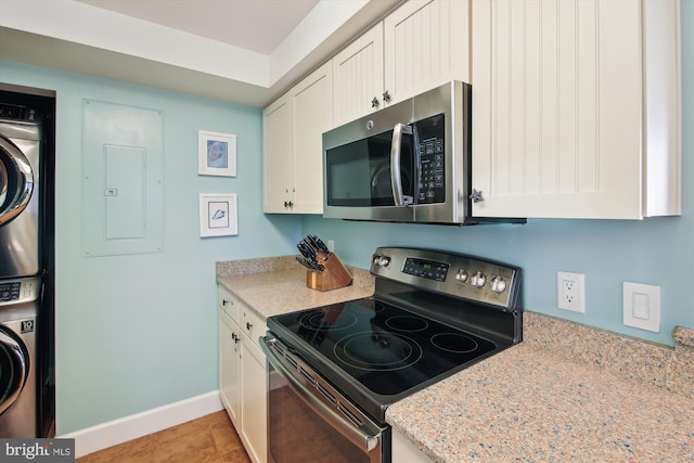 kitchen featuring stacked washer and dryer, stainless steel appliances, electric panel, white cabinets, and light stone counters