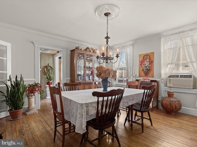 dining area with wood-type flooring, ornamental molding, and a chandelier