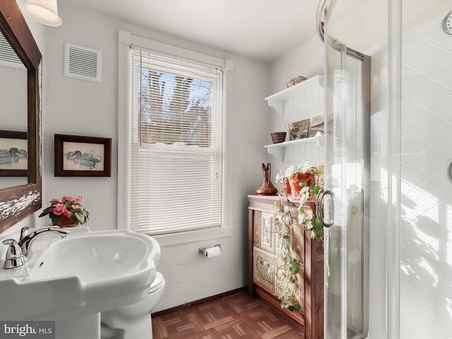 bathroom with parquet floors, a shower with shower door, and sink