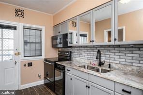 kitchen with light stone countertops, gray cabinetry, crown molding, black appliances, and sink