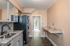 kitchen with sink, dark wood-type flooring, black fridge, light stone counters, and crown molding