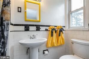 bathroom featuring toilet, tile walls, and a wealth of natural light