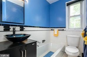 bathroom featuring a bathing tub, vanity, tile walls, and toilet