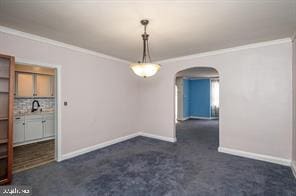 unfurnished dining area featuring dark carpet and crown molding