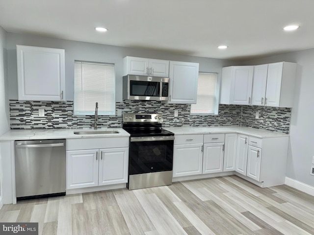 kitchen featuring sink, stainless steel appliances, tasteful backsplash, white cabinets, and light wood-type flooring