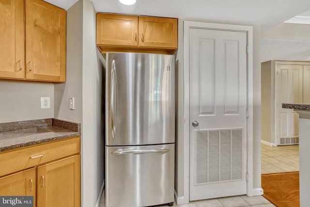 kitchen with dark stone countertops, light tile patterned floors, and stainless steel refrigerator