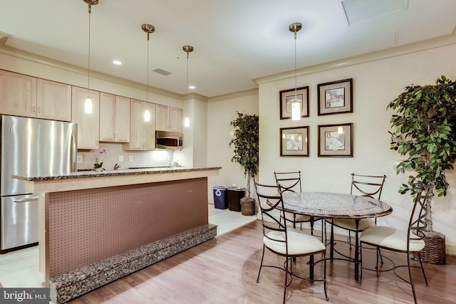 kitchen featuring light brown cabinetry, ornamental molding, stainless steel appliances, pendant lighting, and dark stone countertops