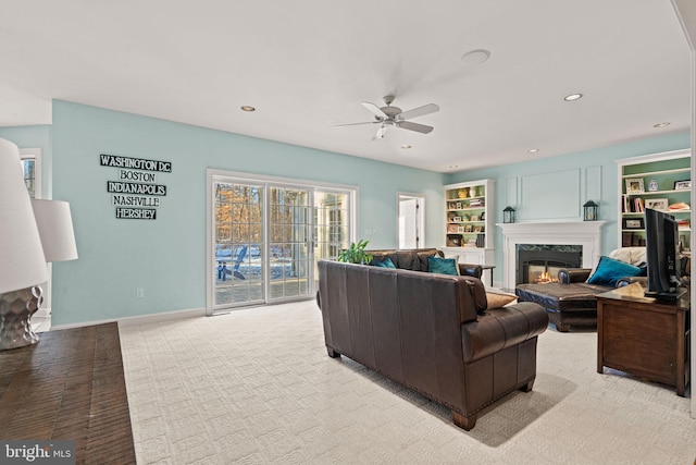 living room with ceiling fan, light colored carpet, built in features, and a high end fireplace