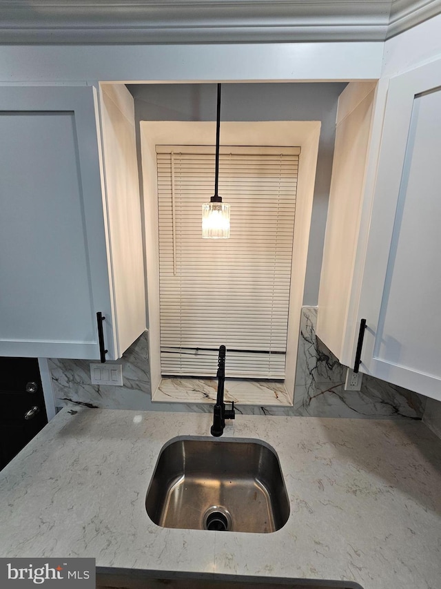 interior details featuring white cabinetry, sink, hanging light fixtures, light stone counters, and decorative backsplash