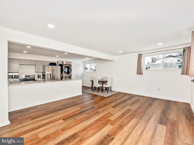 kitchen featuring gray cabinetry, stacked washer and dryer, appliances with stainless steel finishes, and light hardwood / wood-style flooring