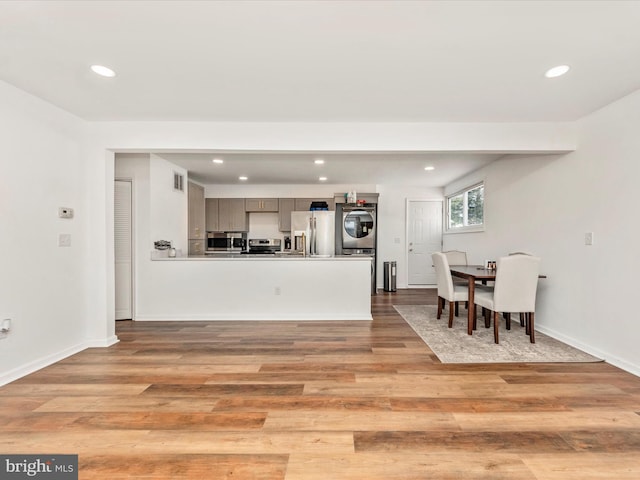 kitchen with kitchen peninsula, stacked washer / dryer, light hardwood / wood-style flooring, and stainless steel appliances