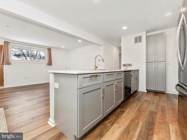 kitchen with gray cabinetry, sink, kitchen peninsula, appliances with stainless steel finishes, and hardwood / wood-style flooring