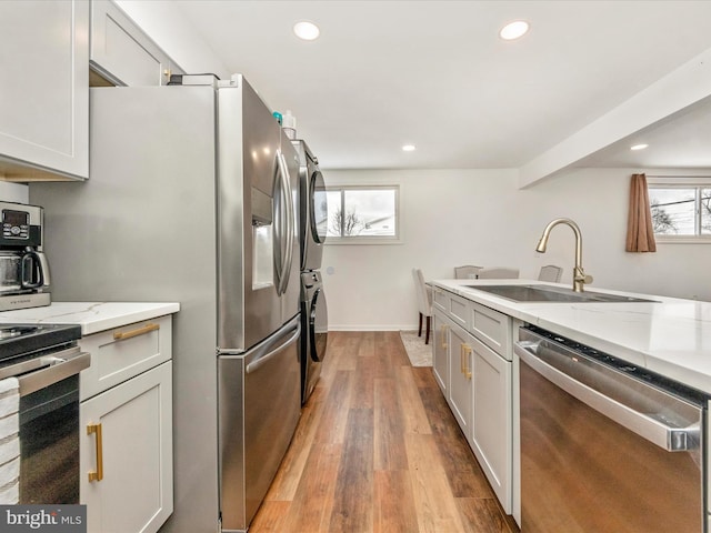 kitchen featuring light stone countertops, appliances with stainless steel finishes, sink, stacked washer / dryer, and light hardwood / wood-style floors