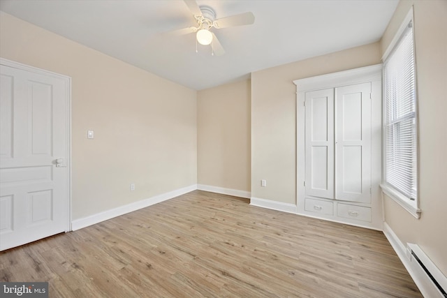spare room with a baseboard radiator, ceiling fan, light wood finished floors, and baseboards