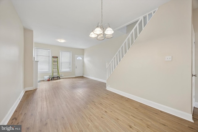 unfurnished living room featuring stairway, wood finished floors, a chandelier, and baseboards