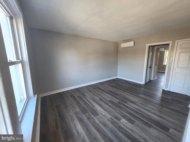 empty room featuring a healthy amount of sunlight, dark wood-type flooring, and a wall mounted AC