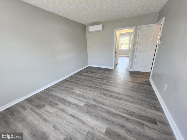 unfurnished room with a wall mounted air conditioner, dark hardwood / wood-style flooring, and a textured ceiling