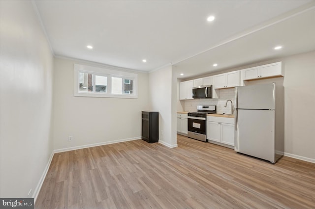 kitchen with backsplash, white cabinets, stainless steel appliances, and light hardwood / wood-style floors