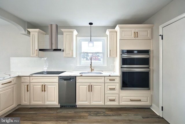 kitchen with sink, wall chimney exhaust hood, stainless steel double oven, light stone counters, and cream cabinets