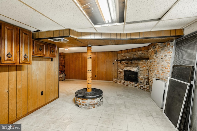 basement featuring a paneled ceiling, wood walls, and a brick fireplace