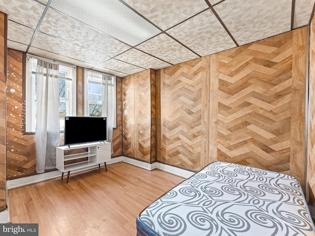 bedroom with a paneled ceiling, wood-type flooring, and wooden walls