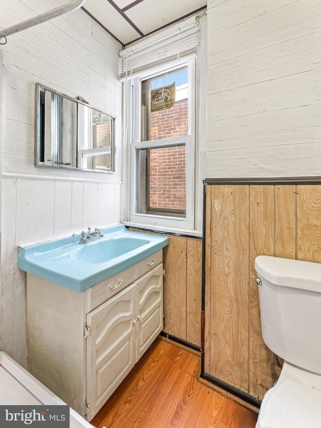 bathroom with hardwood / wood-style floors, vanity, toilet, and wooden walls