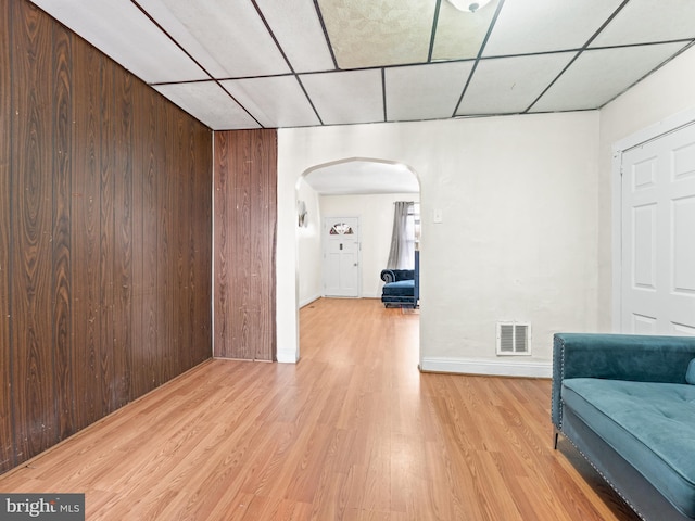 interior space with a paneled ceiling, wooden walls, and light hardwood / wood-style flooring