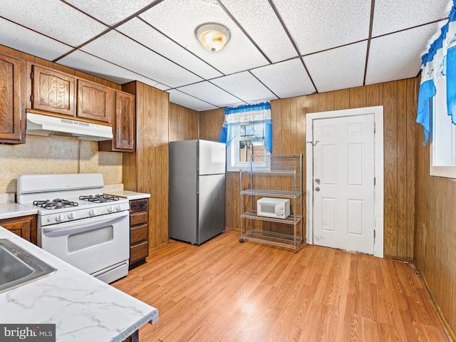 kitchen featuring a drop ceiling, sink, wooden walls, stainless steel fridge, and white gas range