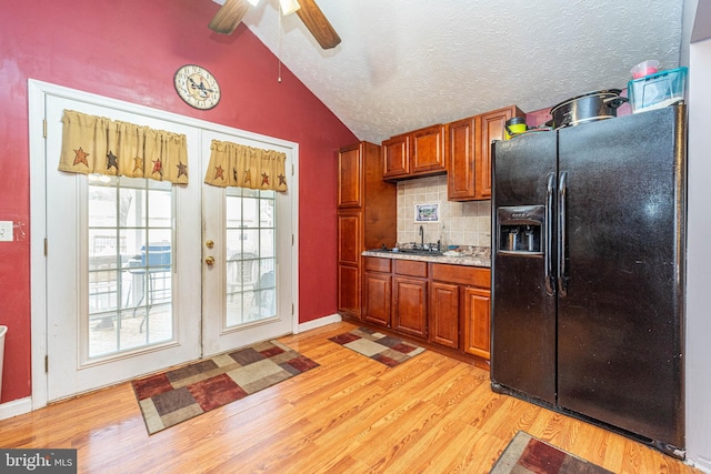 kitchen with light wood-type flooring, backsplash, black fridge, and vaulted ceiling