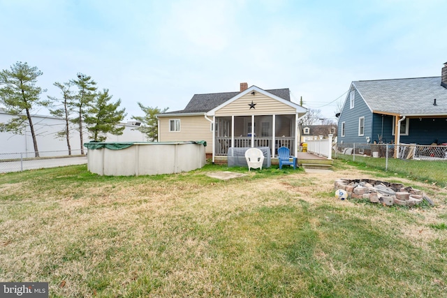 back of property featuring a lawn, a fire pit, a sunroom, and a covered pool