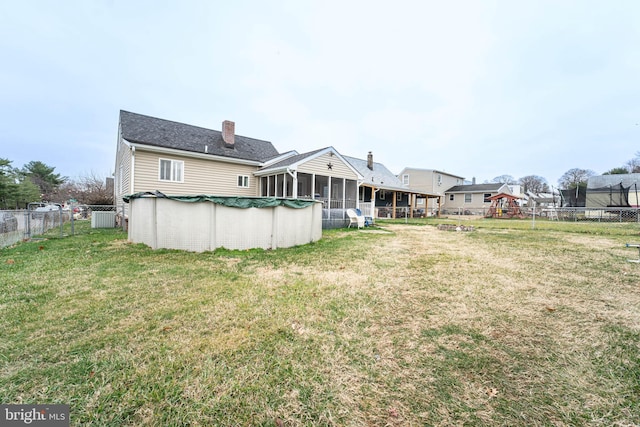 rear view of house featuring a sunroom, a trampoline, a lawn, and a covered pool