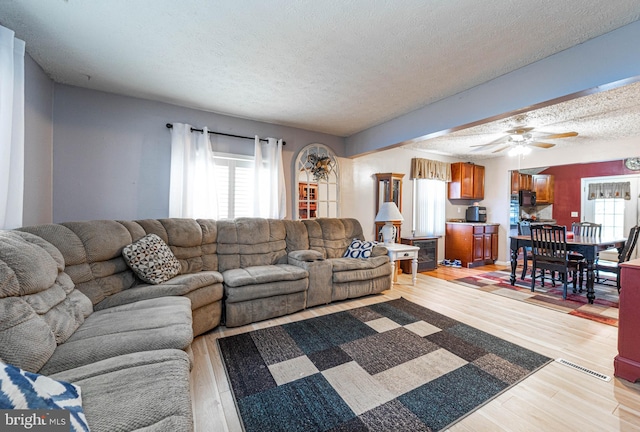 living room with ceiling fan, light hardwood / wood-style flooring, and a textured ceiling