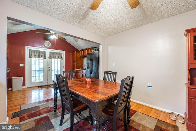 dining room featuring hardwood / wood-style floors, french doors, vaulted ceiling, ceiling fan, and a textured ceiling