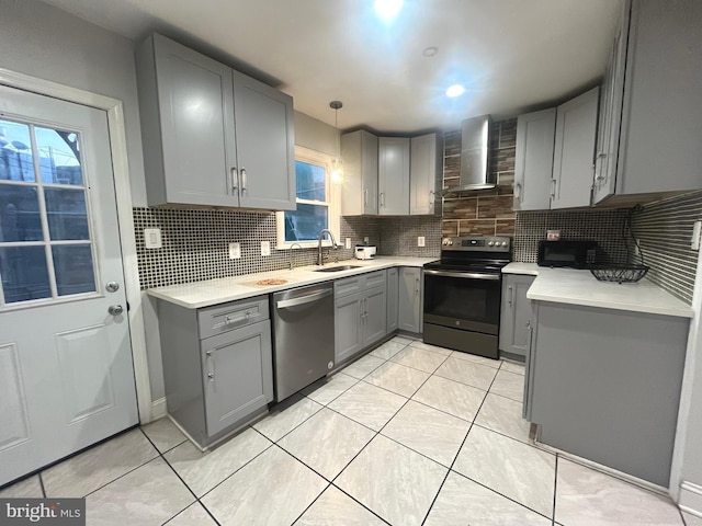 kitchen featuring decorative light fixtures, gray cabinets, wall chimney range hood, and appliances with stainless steel finishes