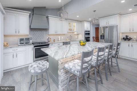 kitchen with appliances with stainless steel finishes, custom exhaust hood, a breakfast bar, white cabinets, and a center island